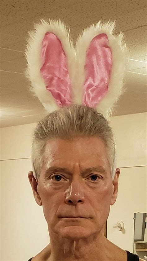 An Older Man With Grey Hair And Pink Bunny Ears On His Head Is Looking