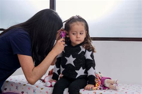 Joven doctora latina revisa el oído de una joven con un otoscopio en su consultorio médico