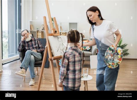 Relaxed Bearded Man In His 70s Looking At Young Ladies Drawing His