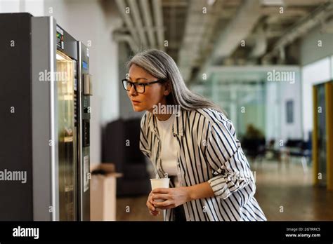 Serious White Haired Mature Woman Using Vending Machine While Drinking