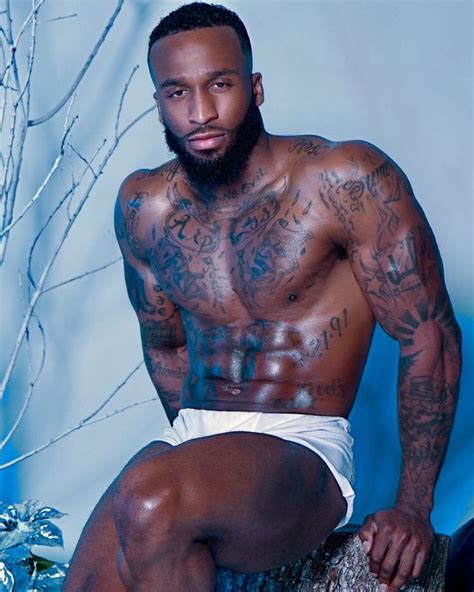 A Shirtless Man With Tattoos Sitting On A Tree Stump In Front Of A Blue