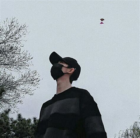 A Man Wearing A Black Hat Looking Up At A Kite Flying In The Sky Behind Him