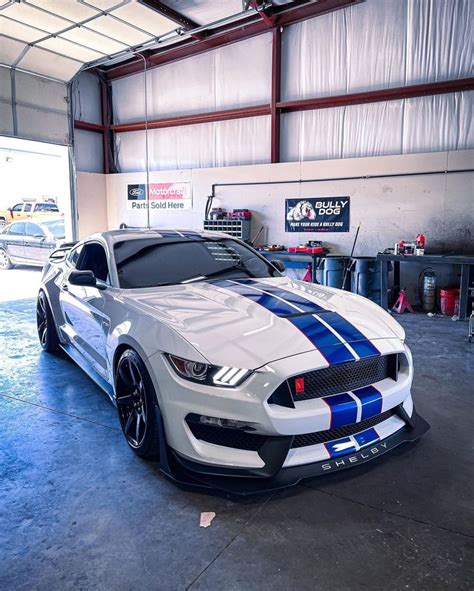 A White Mustang With Blue Stripes Parked In A Garage