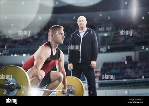 Coach watching focused male weightlifter lifting barbell in arena Stock ...