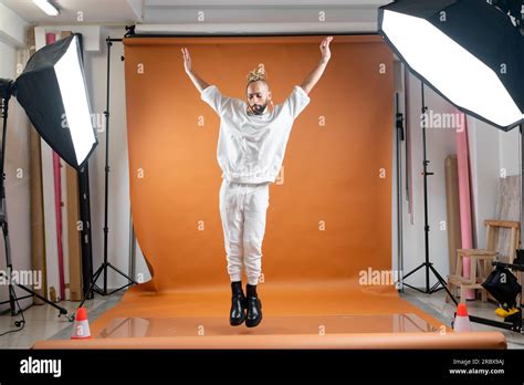 Full Length African American Gay Man With Bright Make Up Jumping Wearing White Dancing On Orange
