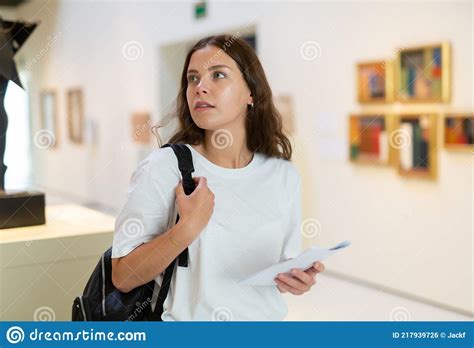 Girl Visitor Examines An Exhibit Standing In An Art Gallery Stock Photo