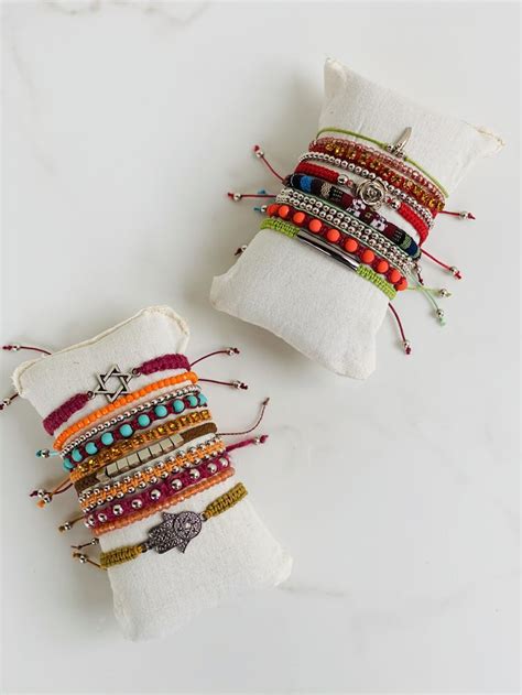 Two White Pillows With Colorful Beaded Bracelets On Them Sitting Next