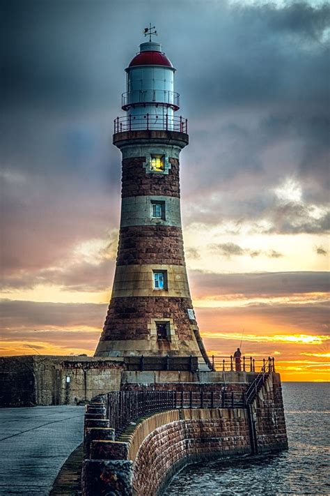 A Light House Sitting On Top Of A Pier Next To The Ocean Under A Cloudy Sky