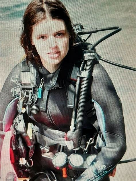 a woman in a diving suit sitting on top of a surfboard and holding onto ...