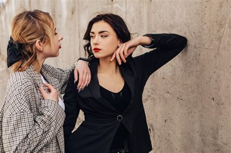 Dos amigas bonitas posando junto a la pared gris pareja de gay lesbianas niñas abrazar