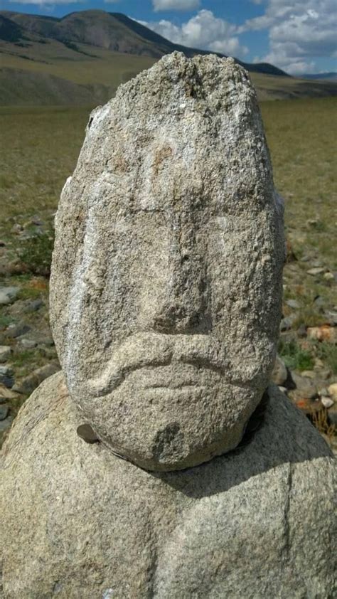 A Rock With A Face Carved Into It In The Middle Of Some Grass And Rocks