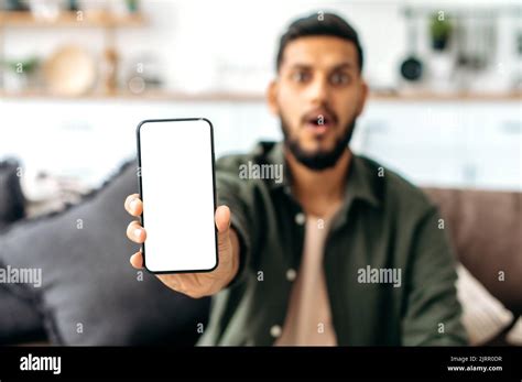 Defocused Shocked Indian Or Arabian Guy In Casual Wear Sits On Sofa In