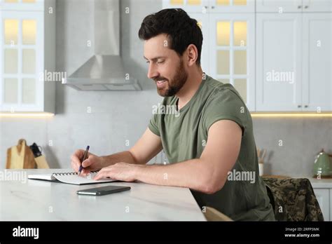 Soldier Writing In Notebook At White Marble Table In Kitchen Military