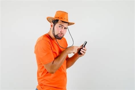 Junger Mann Der Handy In Orange T Shirt Hut Und Nachdenklich Schaut