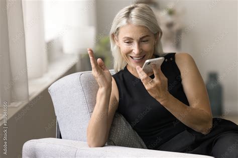 Positive Mature Lady Talking On Speaker On Mobile Phone Call Holding Digital Gadget At Face