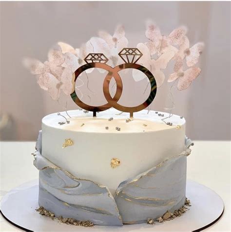 Two Wedding Rings On Top Of A White Cake With Blue Frosting And Gold