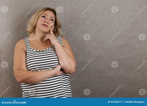 Portrait Of Blonde Plus Size Woman On Grey Background Looking Up And Holding Hand Near Face