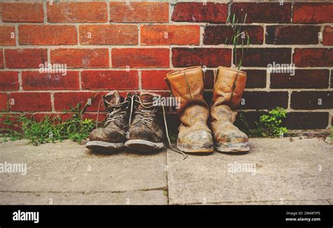 Two Pairs Of Old Boots In Front Of A Brick Wallthe Boots Are Heavily