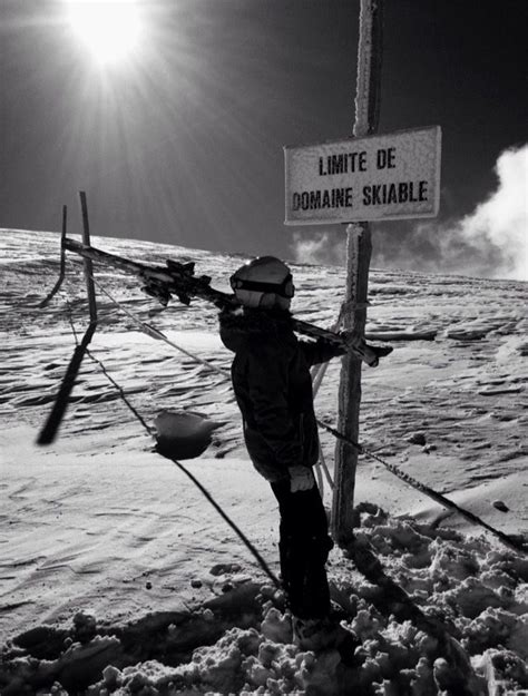 A Man Standing Next To A Sign On Top Of A Snow Covered Slope In The Sun