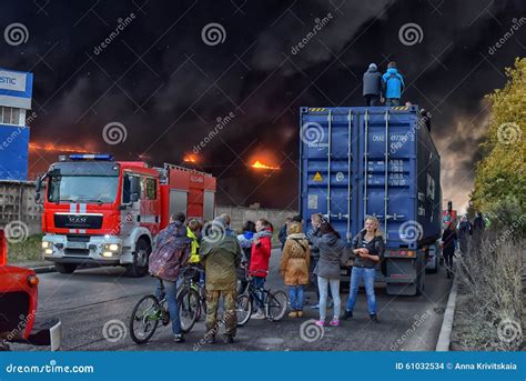 Two Firefighters Watch A Third Fireman Spraying Water On A Store In A