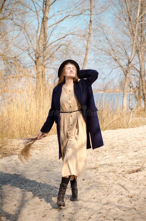Jeune Fille Blonde Du Caucase Dans Un Manteau Et Un Chapeau De Robe Au Printemps Sur La Plage