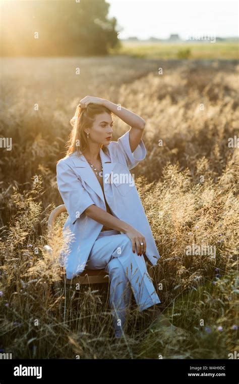 Fashion Photo Of Attractive Blonde Woman In Blue Fashion Suit Sitting On Chair In Wheat Field