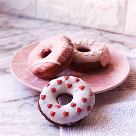 Três Donuts em um prato rosa sobre mesa de mármore e ao fundo parede