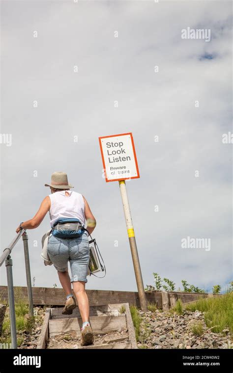 Woman Walking Up Steps To A Footpath To Cross A Railway Track With Sign