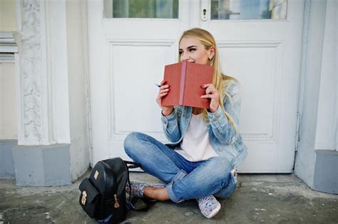 Une fille blonde porte un jean avec un sac à dos posé contre une vieille porte avec un journal
