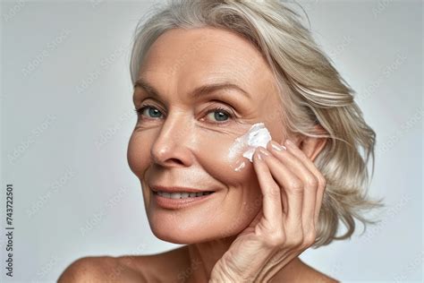 Smiling 50s Middle Aged Mature Older Woman Applying Facial Cream On Face Looking At Camera