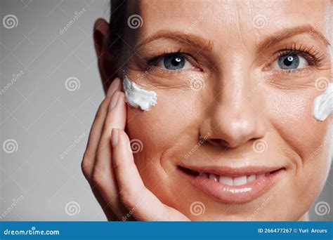 Beautiful Mature Woman Posing With Face Lotion In Studio Against A Grey