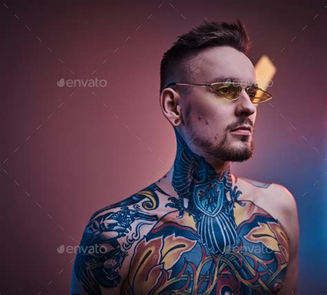 Inked Male Model Posing In A Neon Studio With Half Naked Tattooed Body And Sunglasses Stock