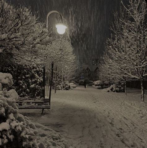 A Snow Covered Park Bench Under A Street Light At Night With The Moon