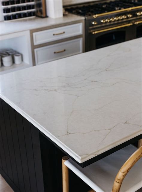 A Kitchen Island With Marble Counter Tops And Wooden Chairs In Front Of