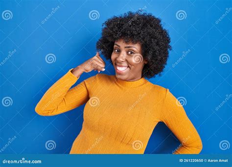 Black Woman With Curly Hair Standing Over Blue Background Smiling Doing Phone Gesture With Hand