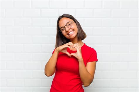 Mulher latina sorrindo e se sentindo feliz fofa romântica e apaixonada fazendo formato de