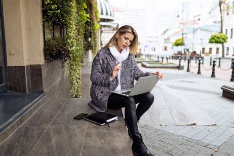 Mature Businesswoman Working On A Laptop Online Sitting On The Steps At The Entrance To The