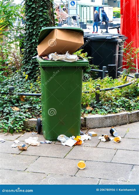 Trash Spills Out Of An Overfilled Trash Can On A Pavement In The City