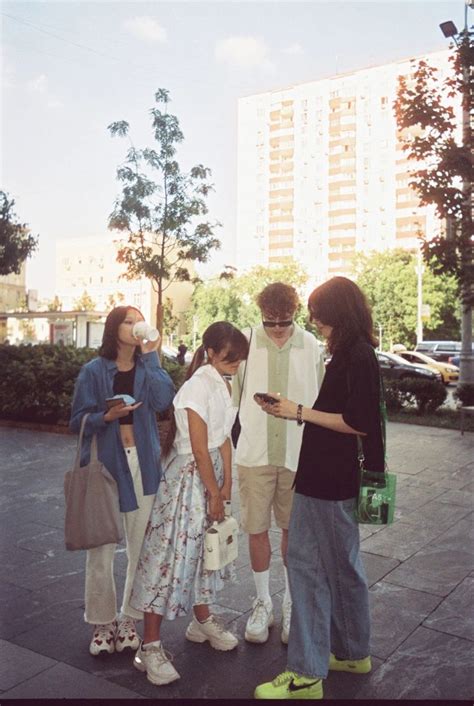 Four People Standing On The Sidewalk Looking At Their Cell Phones