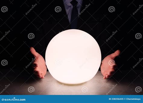 Businessman Using Glowing Crystal Ball To Predict Future At Table In