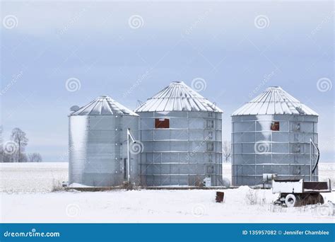 Three Steel Silos Or Grain Bins Covered In Snow On A Farm In A Rural