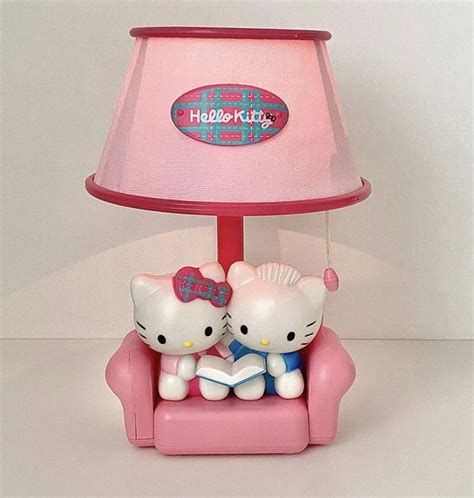 Two Hello Kitty Figurines Are Sitting On A Pink Chair Under A Pink Lamp