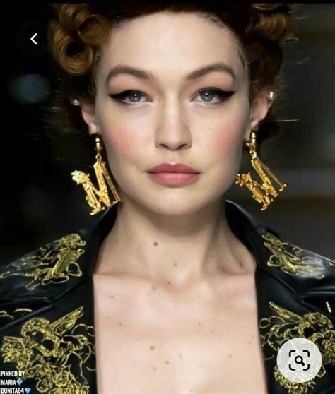 A Close Up Of A Person Wearing Gold Earrings And Black Jacket With An