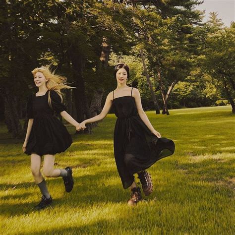 Two Women In Black Dresses Holding Hands And Running Through The Grass