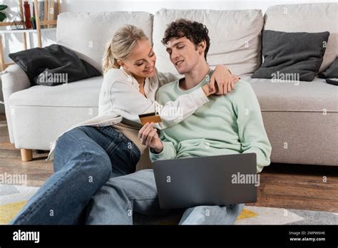 Happy Blonde Woman Hugging Boyfriend Holding Credit Card While Using