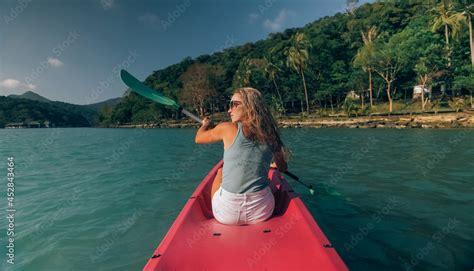 Long Haired Blonde Woman With Sunglasses Rows Bright Pink Canoe Along Sea Bay Water To Beach