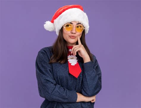 Reflexiva joven caucásica en gafas de sol con gorro de papá noel y