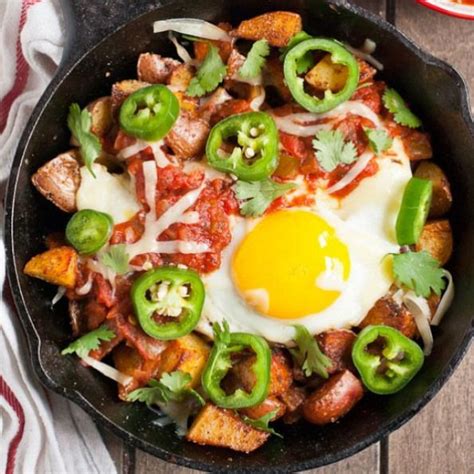 A Skillet Filled With Eggs Sausage And Peppers On Top Of A Wooden Table