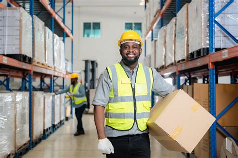 Smiling African Male Warehouse Worker Leaning Against Some Boxes Stock