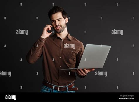 Focused Handsome Guy Talking On Cellphone While Holding Laptop Isolated